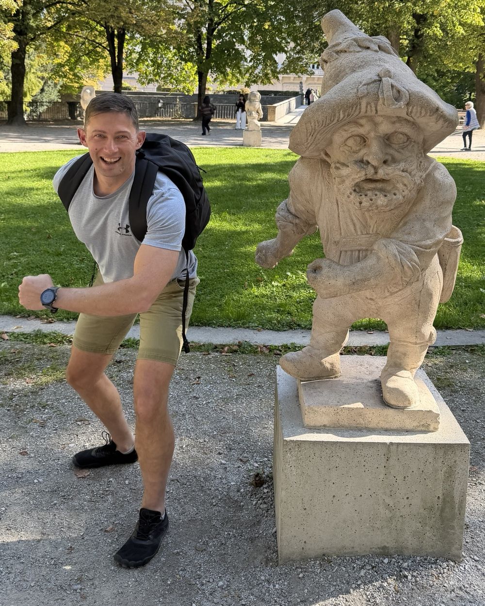 Jaco Blom in a park, grinning and squaring up to a stone dwarf statue on a plinth.