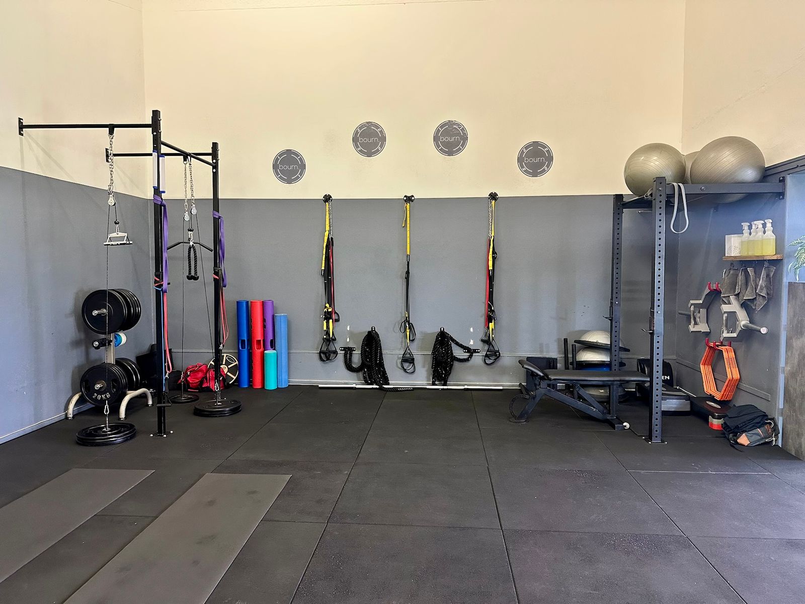 A wall of the studio with a cable rig, suspension trainers, battle ropes, foam rollers and an adjustable bench.
